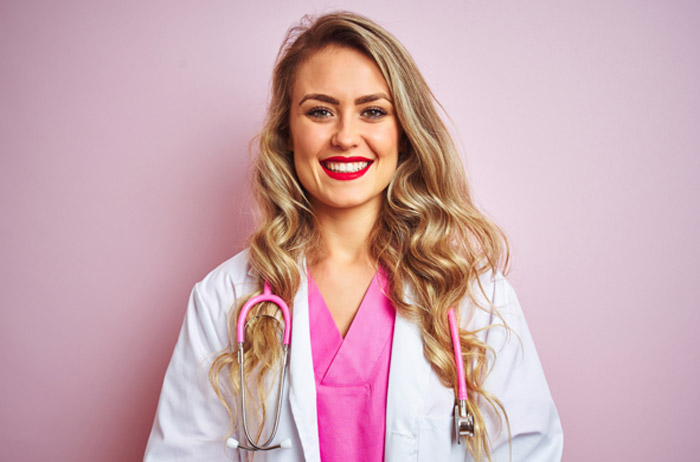 Unsere Kooperationen sind sorgfältig ausgewählt. Nur die besten Frauenärzte und Kliniken haben eine Chance auf eine S-Pap Kooperation.	 Ärztin vor hell-lila Hintergrund mit langen gelockten blonden Haaren im weißen Kittel und Stethoskop, sie lächelt mit Freude und Selbstbewusstsein den Kooperations-Partnern zu.
