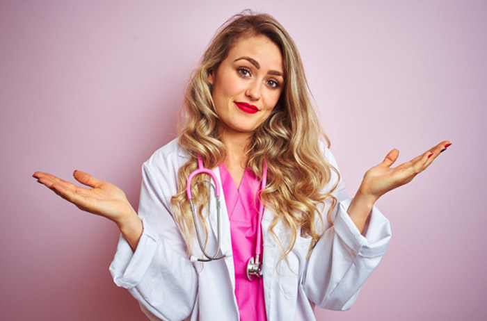 In der Vergangenheit hatten wir Kooperationen mit Frauenärzten und Kliniken, um die Problemfelder bei der Vorsorge besser kennen zu lernen. Daraus haben wir Lösungen entwickelt, die Frauen helfen, gesund zu werden und gesund zu bleiben. Alte Kooperationen haben wir beendet, wenn der Mindestanspruch an einen Frauenarzt nicht erfüllt wurde: Sein Bemühen, Krebsvorstufen nicht zu übersehen, frühzeitig zu erkennen und schonend zu behandeln. Ärztin vor hell-lila Hintergrund mit langen gelockten blonden Haaren im weißen Kittel und Stethoskop, die ihre geöffneten Hände in Schulterhöhe nach rechts und links von sich streckt und die Geste "Tut uns leid" ausdrückt.