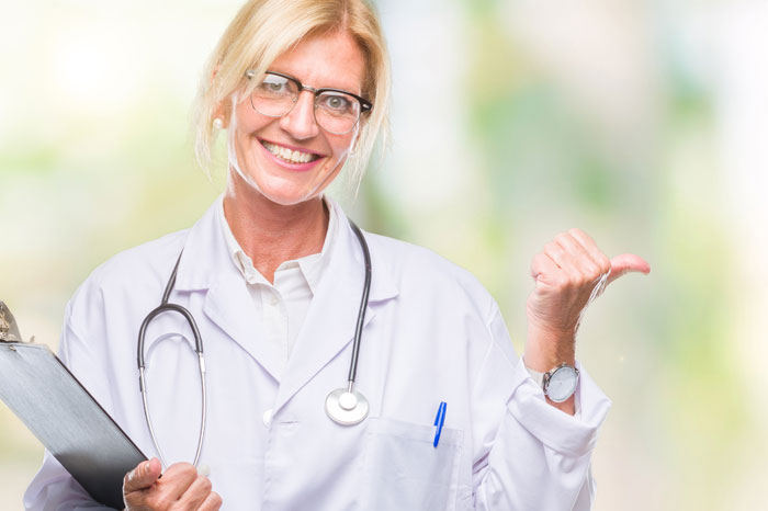 Die Anwendung des S-Pap erhöht die Vorsorgequalität. Kommen Sie Ihrer Verantwortung bei der Krebsvorsorge nach und verwenden Sie den S-Pap für eine sicherere Früherkennung von Gebärmutterhalskrebs. Es ist stets Zeit, mit dem Besseren zu beginnen. Freundlich lächelnde Ärztin mit blonden Haare und Brille, im Kittel mit Stethoskop und Schreibbrett vor gelb-grünen Hintergrund, hebt linke Hand in Schulterhöhe und streckt Daumen seitlich hoch.