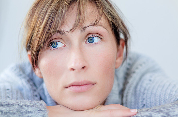 Was macht es für einen Sinn auf fehlerhafte Befunde zu vertrauen? Wie kann man darauf Entscheidungen für die Gesundheit treffen? Junde Frau mit blonden Haaren und blauen Augen in grauem Pullover vor grauem Hintergrund ist frustriert und nachdenklich, weil sie sich nicht auf ihre Pap-Befunde verlassen kann.