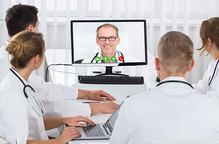 Unterstützung durch Konsile: Patientenbezogene Beratungen von Ärzt*innen durch einen entsprechenden Facharzt. Wir unterstützen bei der Befundmitteilung und Beratung der Patienten. Konsil mit 5 Ärzten, die zu einer Besprechung an einem Tisch zusammengekommen sind und sich Notizen machen.