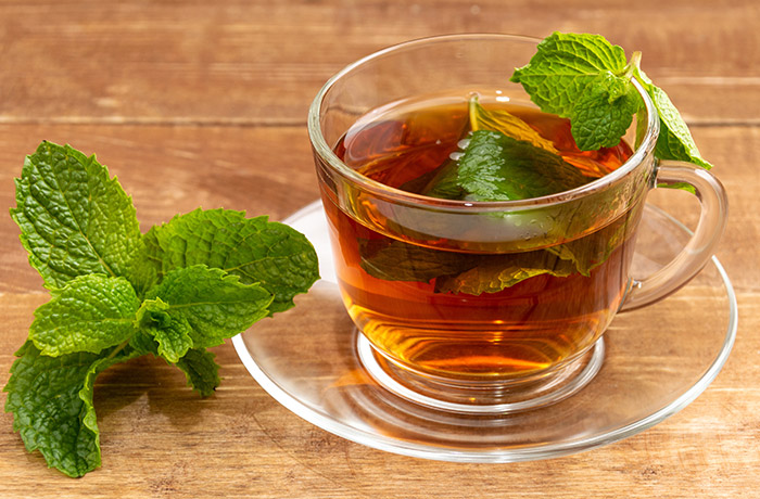 Statt gleich zu operieren kann man der Selbstheilung eine Chance geben. Die konservative Behandlung der Vorstufen von Gebärmutterhalskrebs und deren Heilung ist wissenschaftlich gesichert. Teetasse und Untertasse aus Glas mit schwarzem Tee und frischen Pfefferminzblättern steht auf braunem Holz.