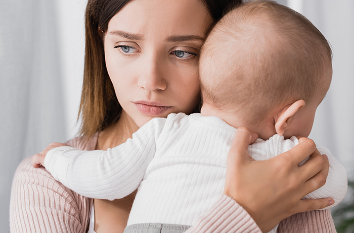 Ein junges Baby und eine erneute Schwangerschaft werden zur Überlastung für die werdende Mutter, wenn unerwartet eine Diagnose von schweren Krebsvorstufen und evtl. sogar Gebärmutterhalskrebs hinzukommt. Junge Mutter mit Baby auf dem Arm schaut ängstlich in die Zukunft.