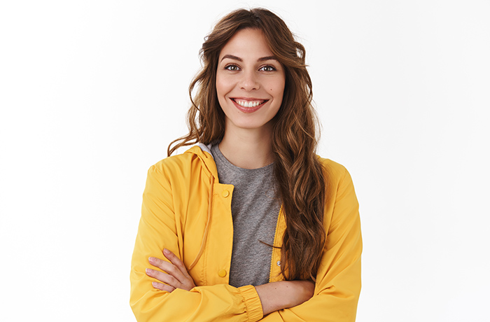 Wenn Sie sich bei der Früherkennung Gebärmutterhalskrebs auskennen und die richtigen Entscheidungen treffen, haben Sie beste Chancen, gesund zu bleiben und gesund zu werden. Junge Frau mit langen braunen Haaren in gelber Jacke schaut optimistich auf die Situation.